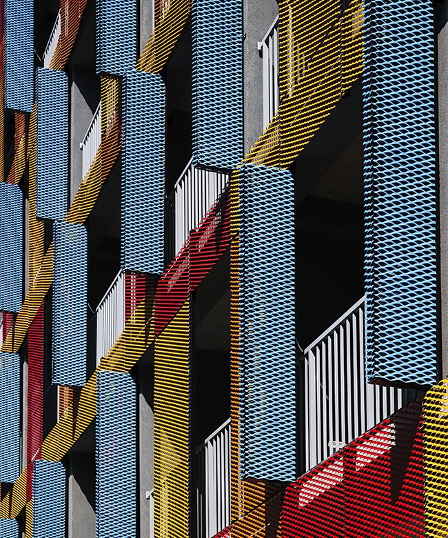 Foto da fachada de um prédio, repleta de estruturas metálicas vazadas e pintadas de cores fortes