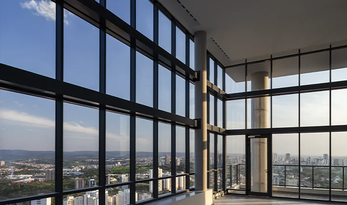 Foto da sala de estar de uma das unidades do prédio Ícone PLaneta, em que as paredes são todas as vidro. É possível ver toda a cidade no horizonte<span height=
