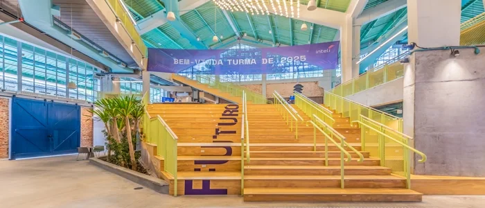 Escada central da Inteli, com degraus em madeira – cada um com uma letra, formando a palavra “futuro”. Ao fundo, a faixa de boas-vindas para os alunos