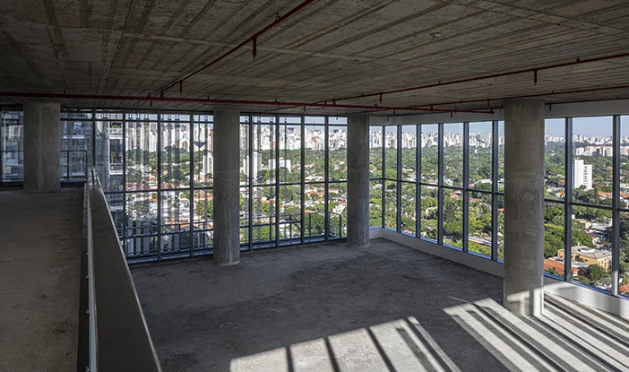 laje corporativa do Edifício Waldy Beira, com pé-direito duplo de seis metros. Na foto, a laje de concreto aparente está sem revestimentos e as paredes são todas de vidro, criando uma grande vista da cidade<span height=