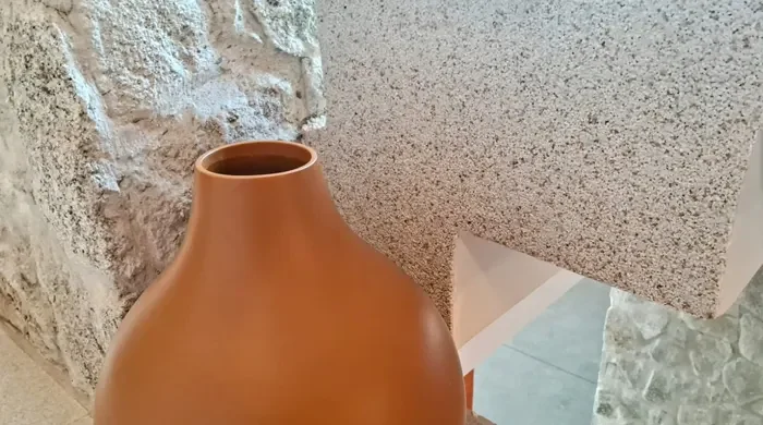 Imagem de um vaso de cerâmica ao lado de uma parede com revestimento T&C ARCH NATURALI, destacando a combinação de texturas e cores.