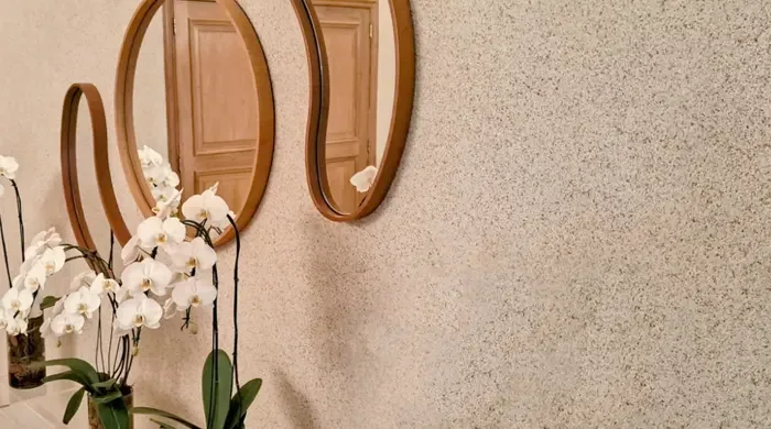 Imagem que destaca a textura T&C ARCH NATURALI na parede, com espelhos circulares e plantas orquídeas, criando um ambiente elegante e harmônico.