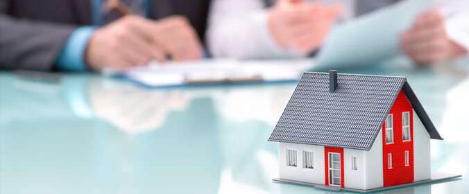 imagem de uma casa em miniatura e duas pessoas com papeis e caneta na mão ao fundo, como se estivesse fazendo negocios