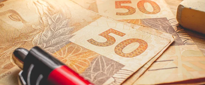imagem de várias cédulas de 50 reais e uma caneta vermelha sobre elas  