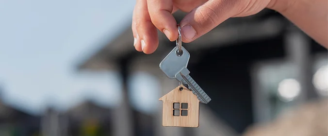 foto de uma mão segurando uma chave, com um chaveiro de casinha feito de madeira