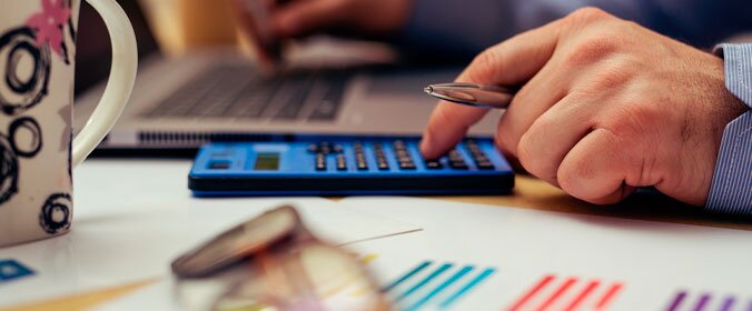 mão masculina segurando uma caneta e digitando em uma calculadora