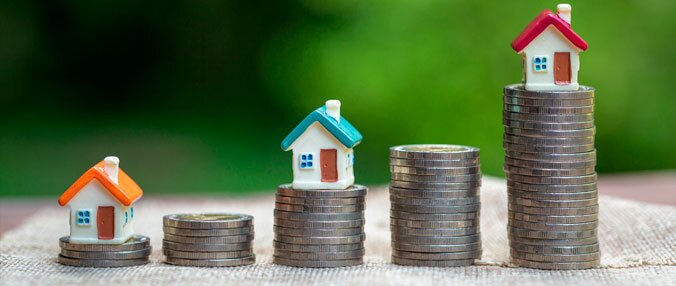 foto de três casinhas de brinquedo, sendo que cada uma delas está sobre uma torre de moedas pratas
