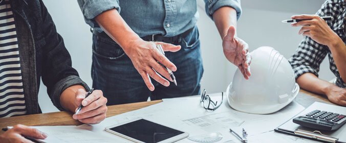 reunião em que só aparece a mão das pessoas e um chapéu de proteção usado em construção ao fundo