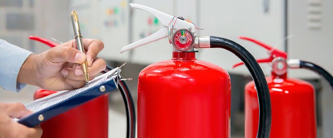 imagem de um extintor e a mão de alguem um pouco mais a frente, segurando uma prancheta e uma caneta