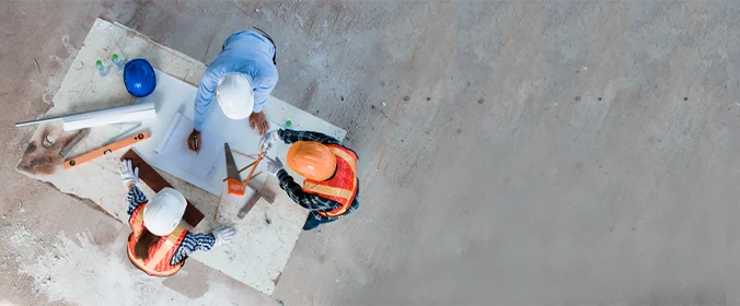 foto de tres pessoas inclinadas sobre uma mesa com apetrechos de construção em volta