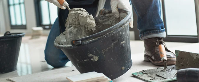foto de uma pessoa mexendo no cimento em um balde, ajoelhada no chão