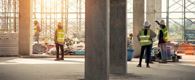 trabalhadores com equipamentos de segurança de um canteiro de obras reunidos em um local com vários materiais de construção espalhados no chão