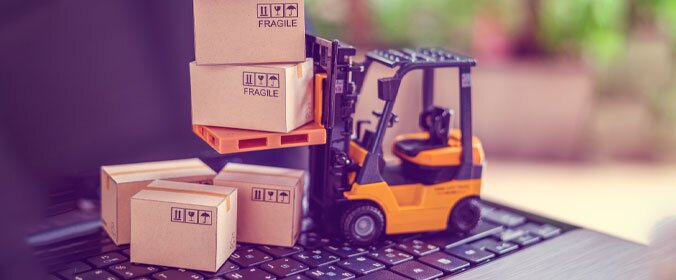 imagem de uma mini empilhadeira com varias caixas pequenas em volta, tudo em cima de um notebook e com um fundo desfocado