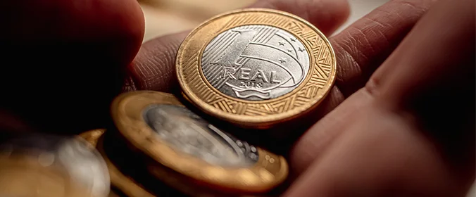 foto de moedas de um real em foco na mão de uma pessoa