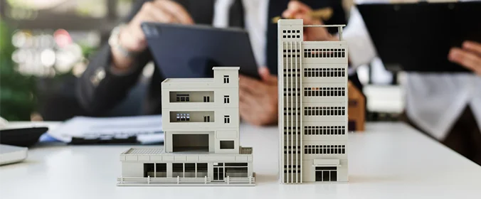 foto de uma maquete de dois prédios e uma pessoa no fundo desfocado