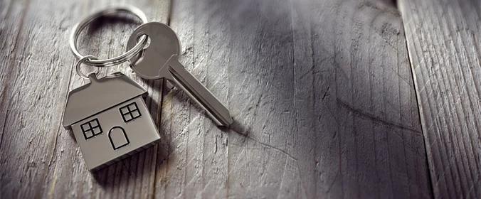 foto de uma chave com um chaveiro de casinha, sobre uma mesa de madeira