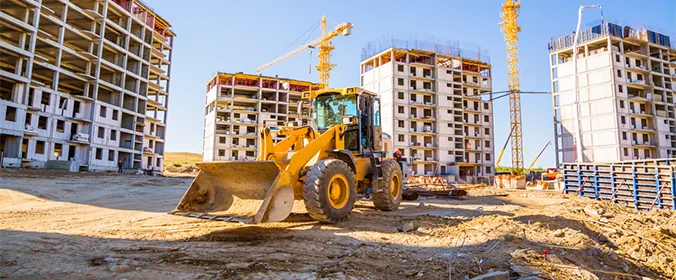 foto de um canteiro de obras com vários prédios ao fundo e um trator em primeiro plano