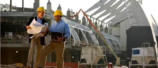 Dois engenheiros com plantas na mão com uma construção atrás