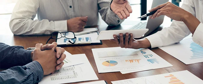 foto de pessoas sentadas ao redor de uma mesa, com várias papéis e notebooks ligados