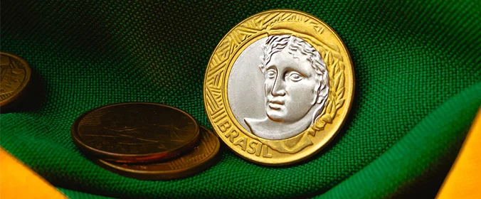 foto de uma moeda de um real em cima de um pedaço da bandeira brasileira