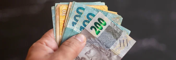 foto de uma mão segurando várias cédulas de 200 e 100 reais