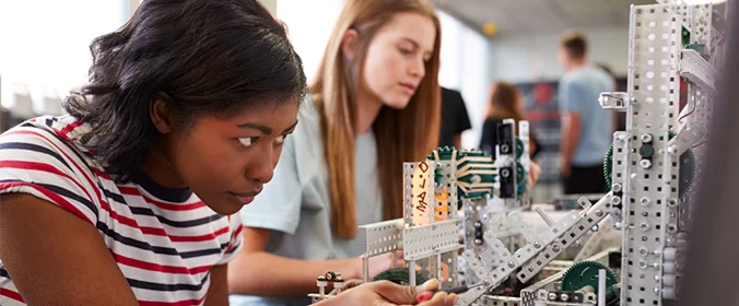 foto de duas mulheres manipulando uma maquete tecnológica de uma ponte , que aparenta ser robotizada