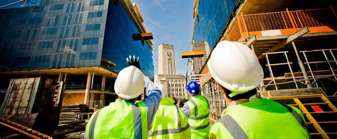 dois trabalhadores da construção em uma grande obra, olhando para cima, na direcao de um edificio muito grande