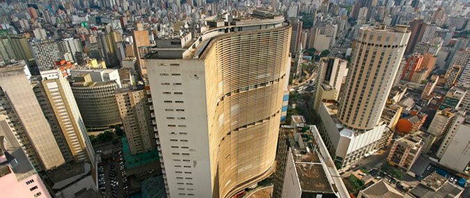 imagem aérea da cidade de são paulo, que destaca o edifício copan. Aparecem vários prédios ao redor