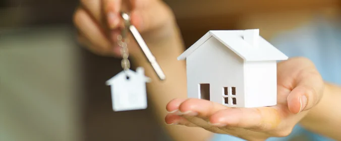 foto de uma pessoa segurando uma casinha de madeira em uma mão e uma chave na outra mão