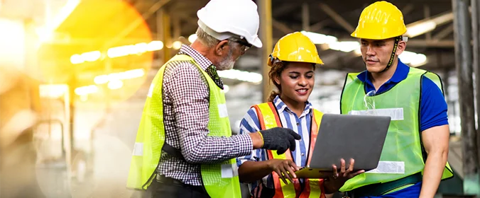 foto de três trabalhadores da construção civil com equipamentos de segurança e a pessoa do meio segurando um notebook