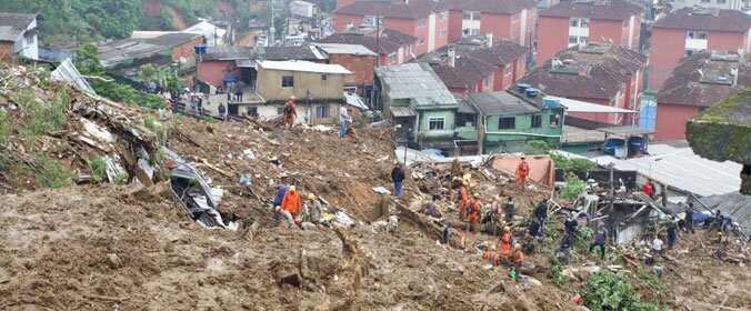 imagem aérea da tragédia em petrópolis, com várias casas destruídas e bombeiros sobre os destroços