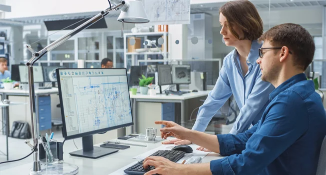 foto de um engenheiro, ao lado de uma engenheira, olhando para a tela de um computador exibinod projetos