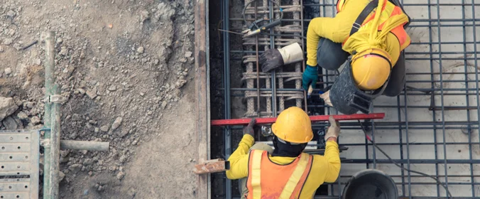 dois trabalhadores do ramo da construção mexendo em uma estrutura. A foto é de uma visão superior