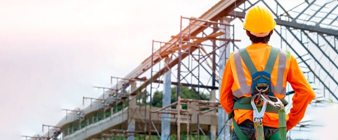 trabalhador de costas completamente equipado com proteções para canteiros de obra olhando para um andaime
