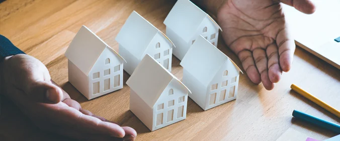 uma pessoa com várias casinhas de madeira em uma mesa, com as mãos em volta