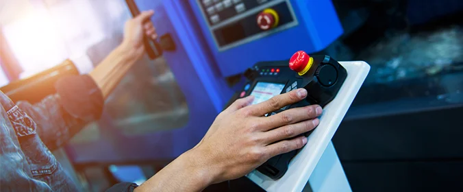 foto de uma pessoa manipulando uma máquina industrial, dando enfoque na mão dela sobre o equipamento de comando