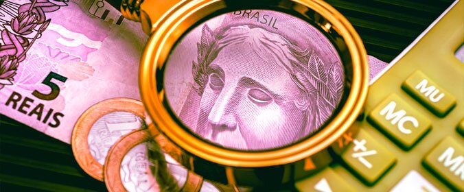 foto de cédulas de 5 reais ao lado de uma calculadora, e uma lupa ampliando o desenho da nota