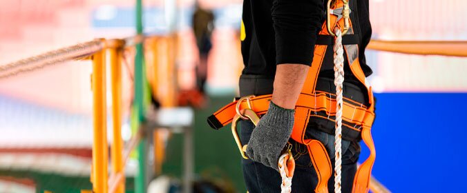 foto de um trabalhador da construção, paramentado com os equipamentos de segurança, e segurando uma corda