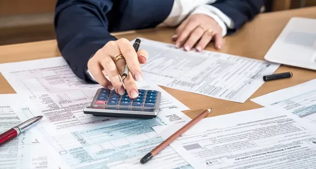 Mulher sentada a mesa e usando calculadora para entender os impactos da reforma tributária nas tendências da construção civil em 2025.