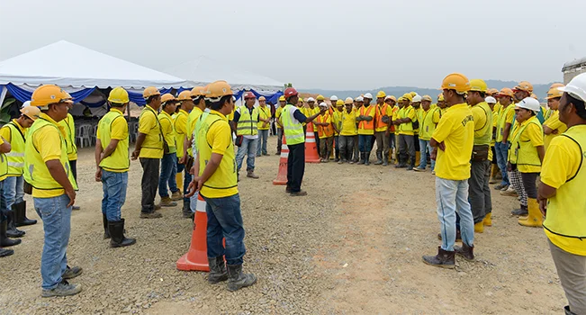 foto de trabalhadores vestidos com equipamentos de segurança e reunidos com uma pessoa falando ao centro