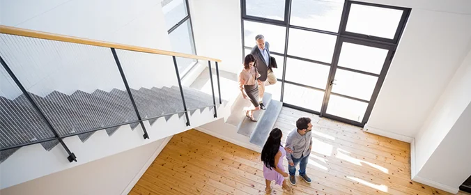 foto de um casal olhando para uma casa sem móveis, acompanhadas de duas pessoas que parecem ser corretores